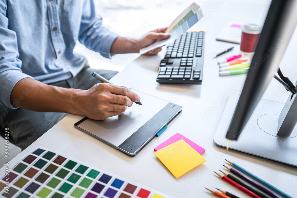 Poster Image of male creative graphic designer working on color selection and drawing on graphics tablet at workplace with work tools and accessories in workspace