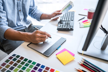 Image of male creative graphic designer working on color selection and drawing on graphics tablet at workplace with work tools and accessories in workspace