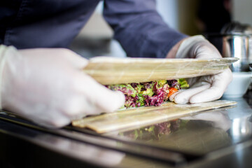 closeup chef preparing salad with eel cucumbers and lettuce leaves on mat