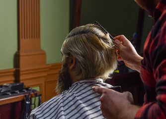 Fototapeta premium Barber and client. Barber works hairstyle for bearded man barbershop background. Guy with long dyed blond hair. Hipster client getting haircut. Professional hairstylist in barbershop interior