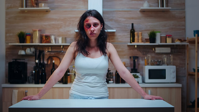 Woman victim screaming and crying desperately sitting in the kitchen. Traumatised abused terrified beaten wife covered in bruises suffering injury from alcoholic aggression brutal drunk man.