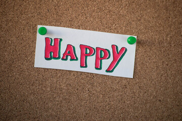 The sign "happy" drawn with red and green marker is attached to the cork board with a green button.