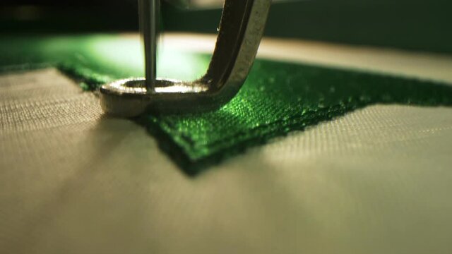 Machine embroiders green detail on hockey uniform in shop