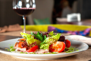 Green salad with tomato and smoked ham. glass of red wine in the background