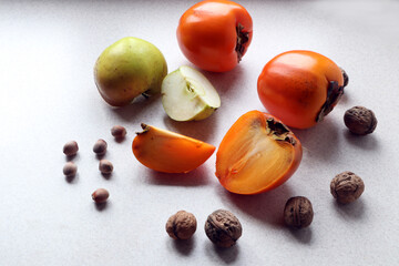  Ripe persimmon and green Apple slices, walnuts and hazel on a light background, side view, close - up-the concept of using seasonal fruits in cooking
