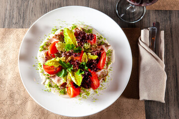Green salad with tomato and smoked ham. glass of red wine in the background. top view. light from the restaurant window