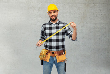 profession, construction and building concept - happy smiling male worker or builder in helmet with ruler over grey concrete background