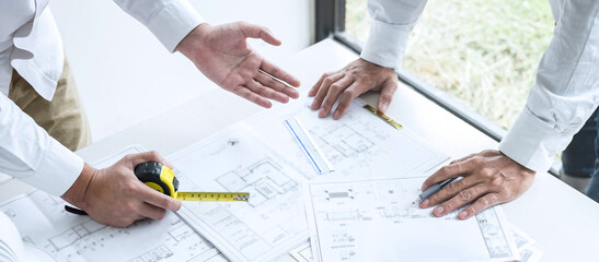 Construction engineering or architect discussing a blueprint and building model while checking information on sketching meeting for architectural project in work site