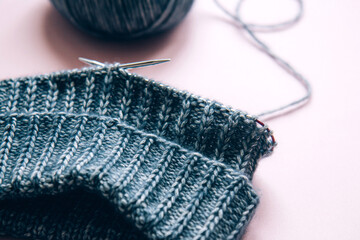 Knitting project underway. Knitting with a ball of aquamarine yarn and knitting needles on pink background. Woman knitting woolen clothes