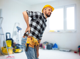 health, construction and repair concept - male worker or builder in helmet having back ache over room with building equipment background