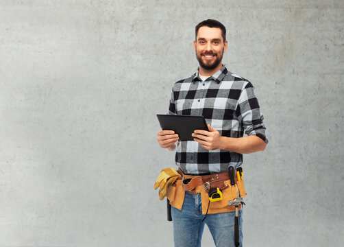 profession, construction and building concept - happy smiling worker or builder with tablet pc computer and tools over grey concrete background