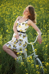 Naklejka na ściany i meble Girl on a white bike in a rapeseed field