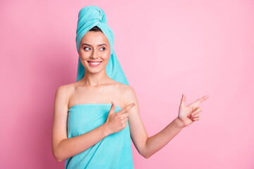 Photo of optimistic cute young lady pointing empty space wear teal bath towels on head body isolated on pink color background