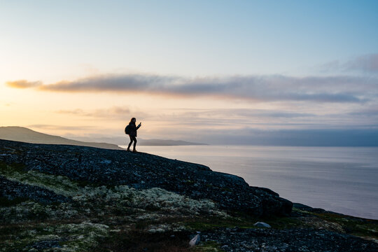 Silhouette figure of young woman traveller enjoying the Beaty of nordic nature on the mountain near the sea taking the picture of the sunset 