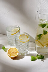 drink, detox and diet concept - glasses with fruit water or lemonade, lemons, limes and peppermint on white table