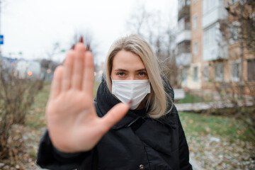 Young woman in medical face mask showing STOP gesture. Portrait of a girl outside in winter, selective focus on the face