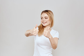 cheerful blonde in a white t-shirt gesturing with her hands light background