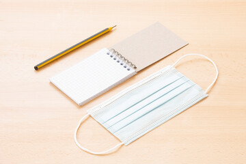 A face mask and a blank spiral notepad with a pen are arranged on a wooden table. To-do list concept during the Covid-19 Outbreak.