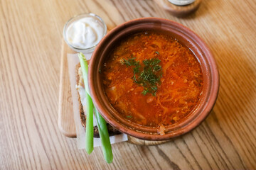 Ukrainian borscht with bacon bread sour cream and herbs on a wooden table in the dining room