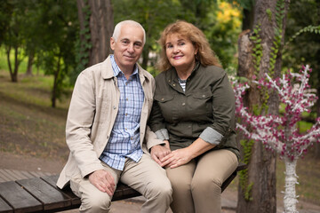 Fototapeta premium Senior elder couple together in park in autumn. Wife hugging husband smile with happiness. Beautiful love relation and care of retirement old people.
