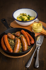 Oldenburger Grünkohl mit Pinkel, Kohlwurst, Senf und Kartoffeln in Gusseisen Pfanne auf Holz Tisch