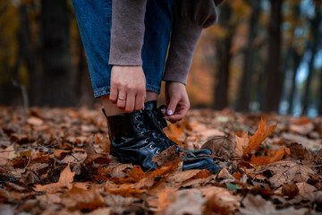 Woman legs in black boots and blue jeans walking  in autumn park. Yellow and orange foliage on the background 