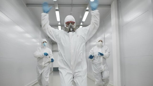 Team of medical workers in hazmat suits dancing and walking in hospital corridor