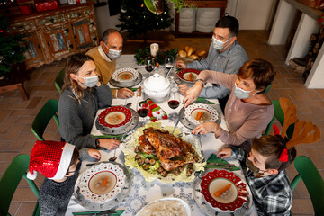 Zenith angle of a Family gathered around the table at Christmas Thanksgiving dinner on 2020. Family members wear surgical masks to comply with the new health regulations. Covid quarantine, lockdown.