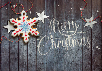 Merry Christmas wishes and festive decoration on wooden background. Snowflake shaped gingerbread cookie.