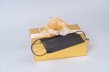 Gold gift box with surgical face mask. Christmas celebration with social distancing to protection COVID-19