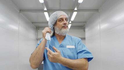 Portrait of happy aged surgeon removing safety mask walking in hospital corridor