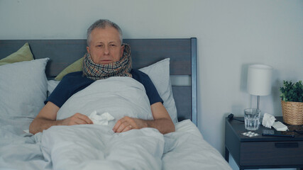 A sick man is lying in bed and coughs and has a runny nose.