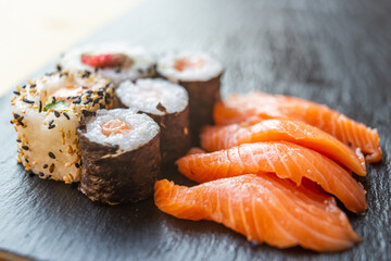 Sushi, uramaki, rolls and sashimi on a slate tray.