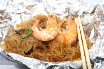 Baked Shrimp with Glass Noodles, a traditional Thai food wrapped in heat-treated freud paper and chopsticks, ready to serve-eat on a white background.