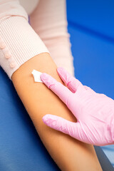 Hand of nurse applying cotton swab to arm of young woman after blood sample in the hospital