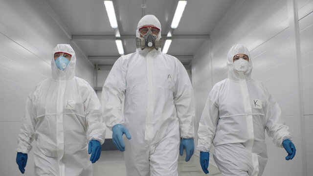 Team of virologists in hazmat suits walking in corridor to do disinfection