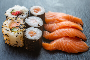 Sushi, uramaki, rolls and sashimi on a slate tray.