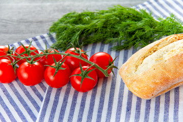 Bread roll, cherry tomatoes and dill on a napkin. Dark background. Top view, close-up.