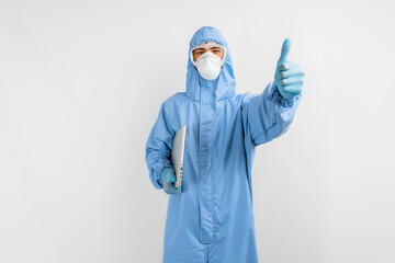 Fototapeta na wymiar man doctor in a protective medical suit to protect against coronavirus, in a mask, glasses and gloves, with a laptop shows a thumb up, on a white background, healthcare