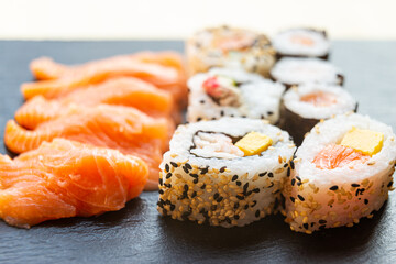 Sushi, uramaki, rolls and sashimi on a slate tray.