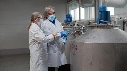 Senior woman and man specialists in safety mask and gloves making inspection of production line