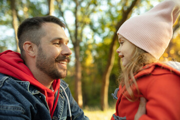 Smiling. Happy father and little cute daughter walking down the forest path in autumn sunny day. Family time, togehterness, parenting and happy childhood concept. Weekend with sincere emotions.