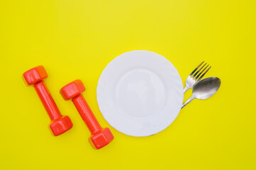 Red dumbbells and a white plate on a yellow background. Sports nutrition.