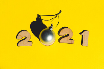 Numbers 2021 from wooden letters and christmas ball on a yellow background.