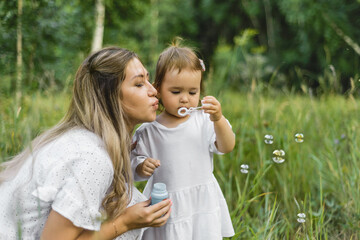 a mother blows soap bubbles for a child in the Park. mother plays with her daughter in nature. happy childhood