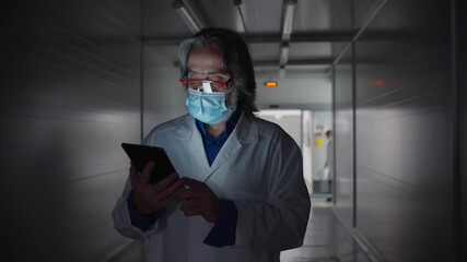 Fototapeta na wymiar Senior male doctor using tablet computer walking in hospital corridor