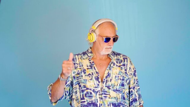 Grandfather funny caucasian dancing going crazy and clubbing listening music using headphones isolated on blue background 
