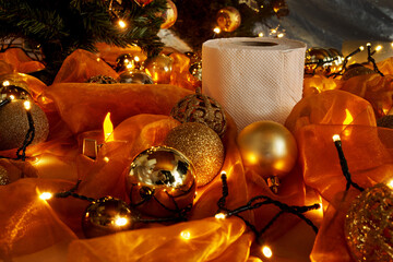 a roll of toilet paper is lying on orange cloth next to a christmas tree and is surrounded by golden christmas balls and festive lights