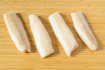 Raw pieces of frozen cod fish loins on wooden cutting board.