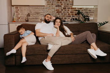 Obraz premium Dad and mom are watching TV on the sofa in the evening. The son is playing a game on a cellphone near his family. Relatives at home.